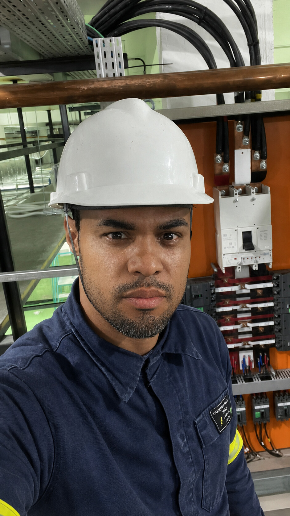 Braga, profissional da Biem Elétrica, com capacete de segurança em frente a um quadro elétrico industrial